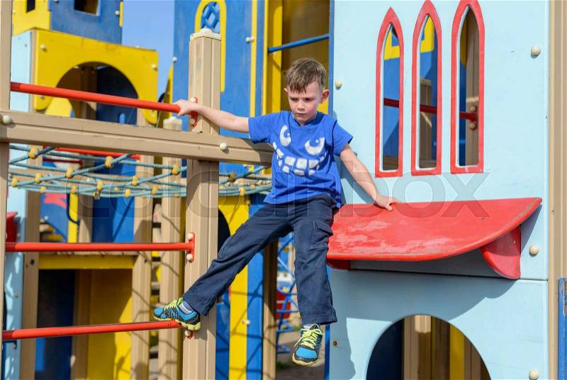 Cute child in blue climbing down ladder pole on colorful little house at playground, stock photo