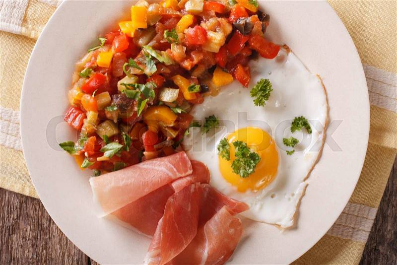 Spanish breakfast: fried egg, ham and pisto on a plate on the table. Horizontal view from above , stock photo