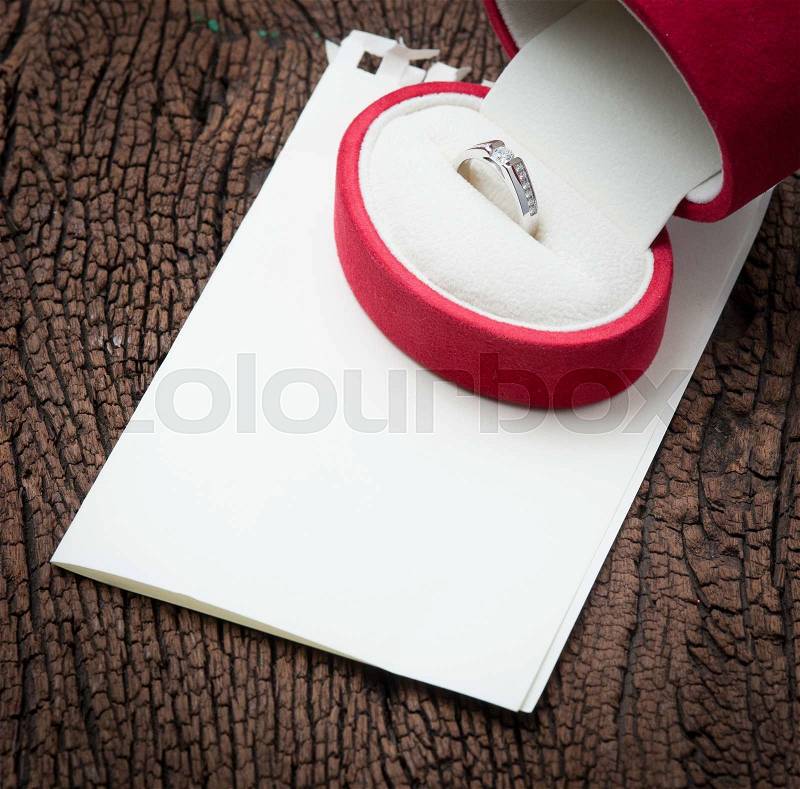 Diamond ring in red velvet box with blank notepaper on wood, stock photo