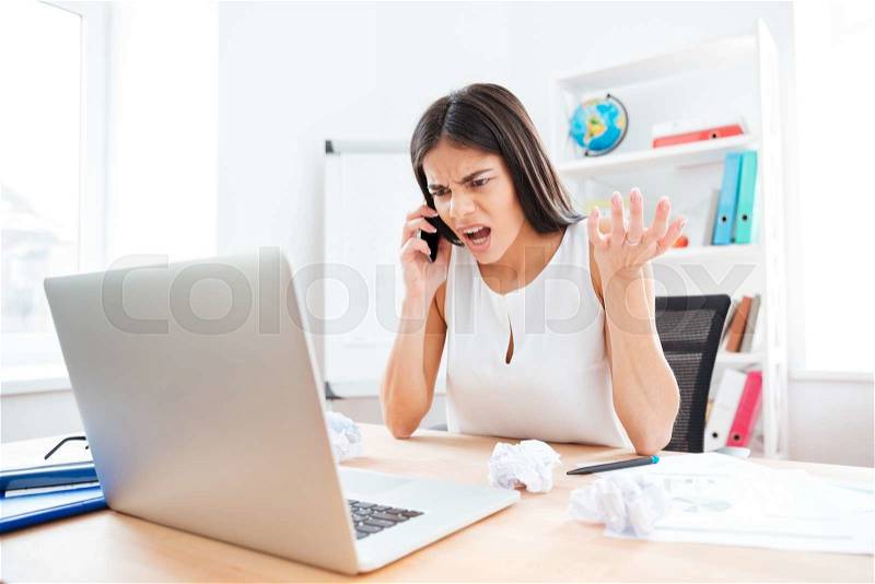 Angry businesswoman talking on the phone in office, stock photo