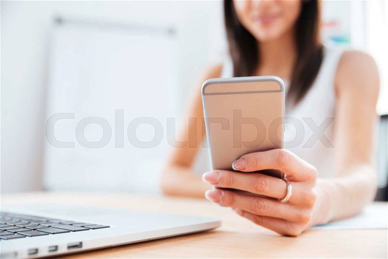 Closeup portrait of a female hands using smartphone in office. Focus on smartphone, stock photo
