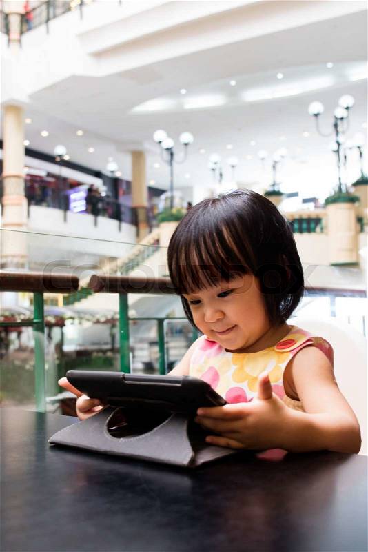 Asian Little Chinese Girl Looking at Digital Tablet in Outdoor Cafe, stock photo