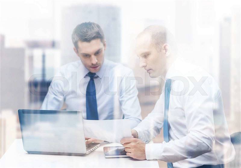Business, technology and office concept - two businessmen with laptop, tablet pc computer and papers having discussion in office, stock photo