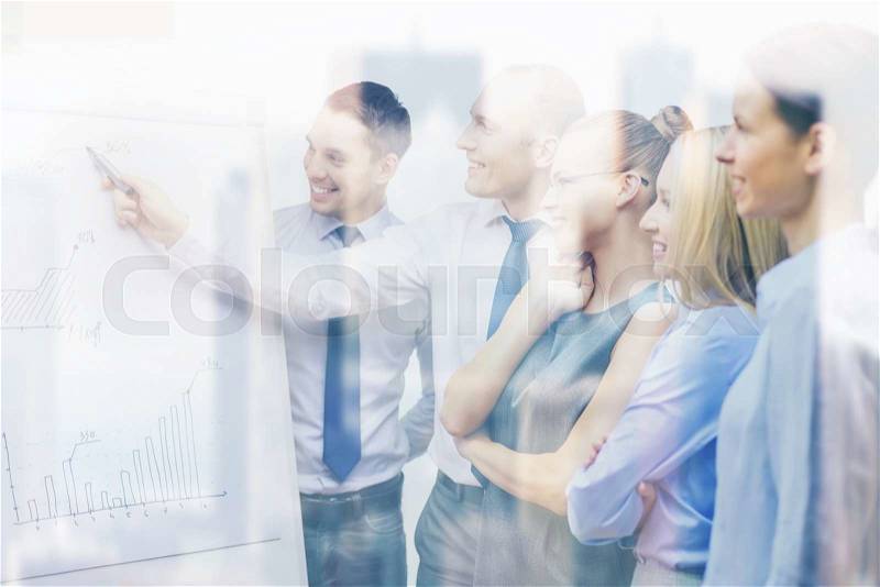 Business and office concept - smiling business team with charts on flip board having discussion, stock photo