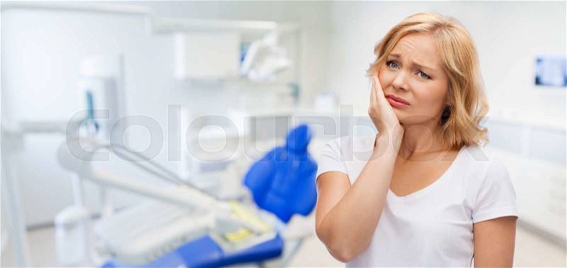 People, healthcare, dentistry and problem concept - unhappy woman suffering toothache over dental office background, stock photo
