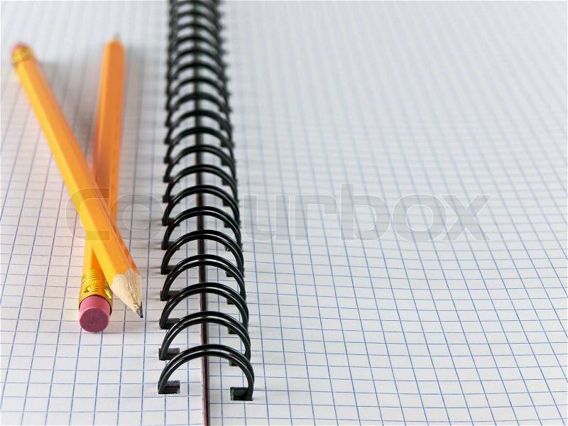 Opened notepad notebook sheet in a cage with two pencils, stock photo