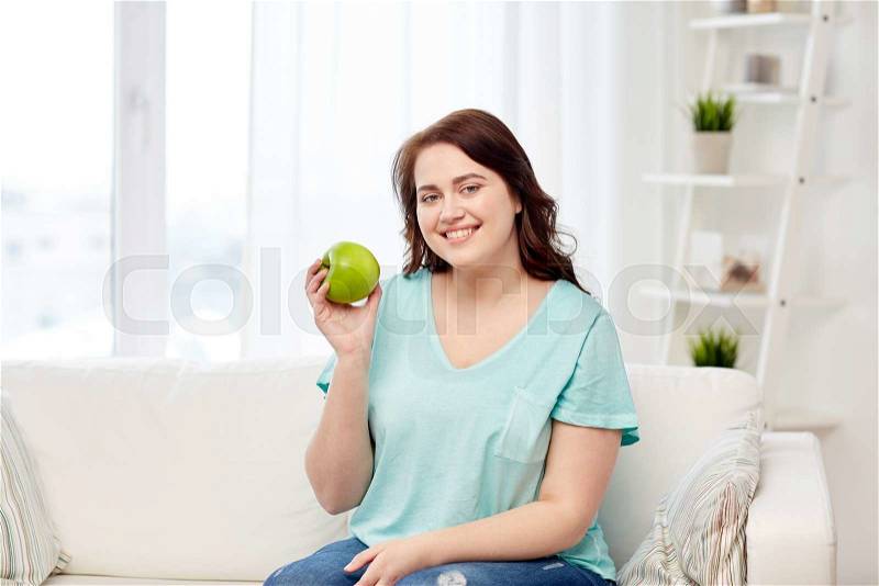 Healthy eating, organic food, fruits, diet and people concept - happy young plus size woman eating green apple at home, stock photo