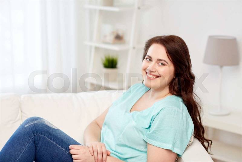 People and leisure concept - happy young woman plus size sitting on sofa at home, stock photo