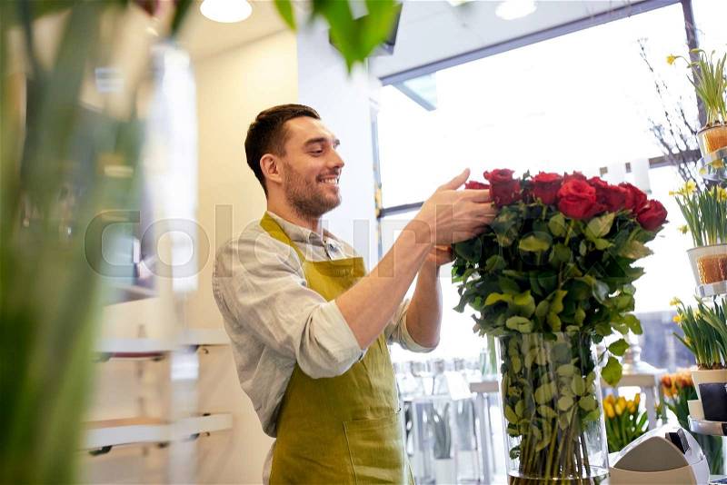 People, business, sale and floristry concept - happy smiling florist man with red roses at flower shop, stock photo