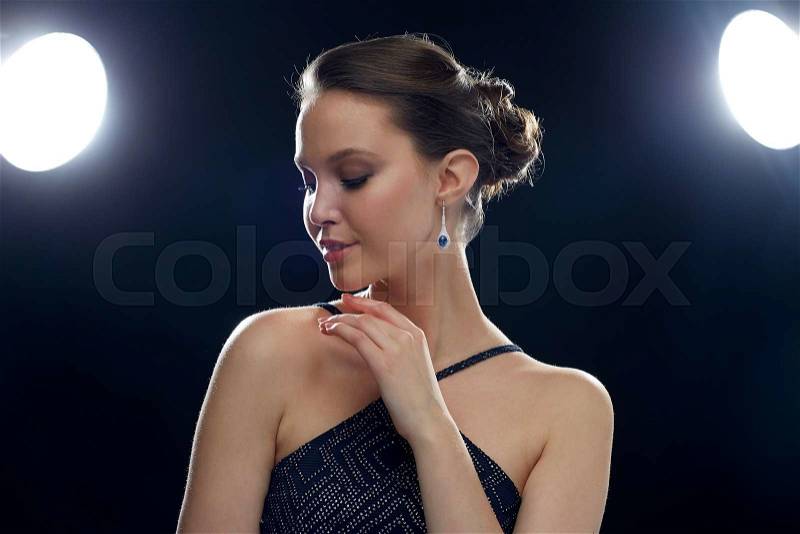 Beauty, jewelry, people and luxury concept - beautiful young asian woman with earring over black background and spotlights, stock photo