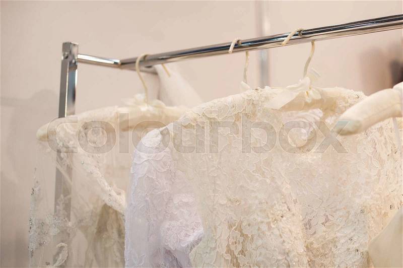 Beautiful white cream wedding dresses made of silk chiffon, tulle and lace hanging on hangers with bows, stock photo