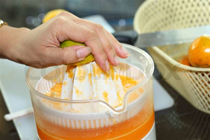 Orange fruit squeezed with woman hand in juicer machine, orange juice, stock photo