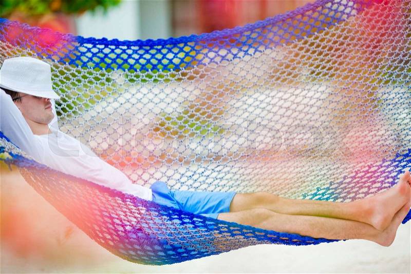 Lazy time. Man in hat in a hammock on summer day at beach, stock photo