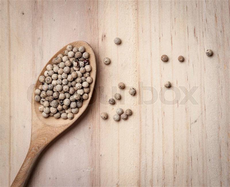 White pepper seeds in spoon on the wood table, stock photo
