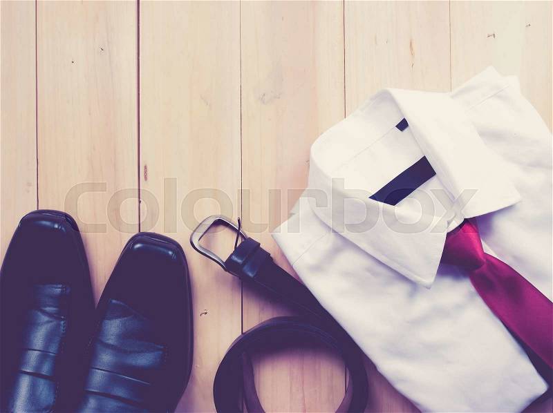 Man\'s style accessories,shirt with a bright tie, shoes and a belt on wooden background,vintage color toned image, stock photo