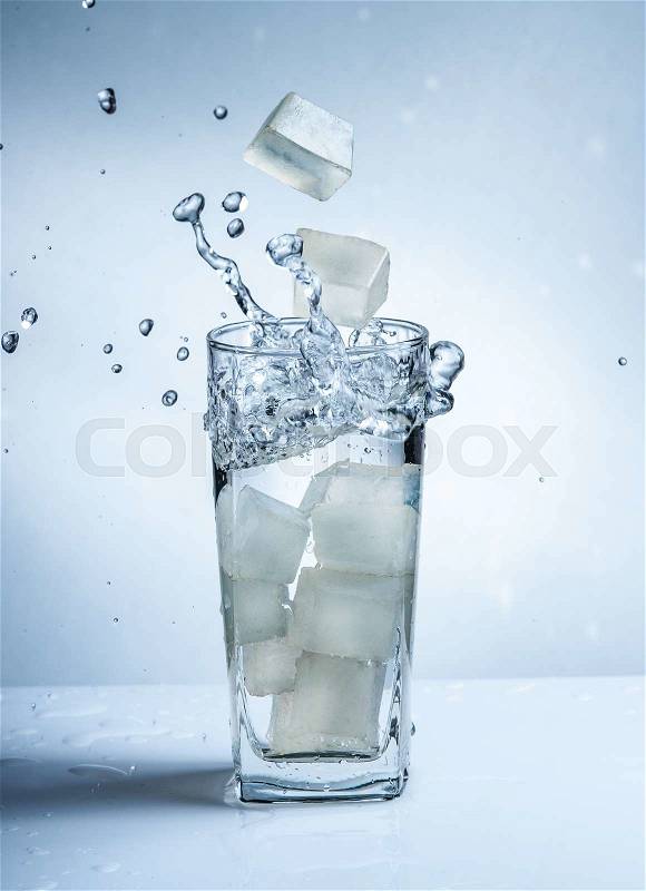 Ice cubes with water splash in glasses on blue background, stock photo