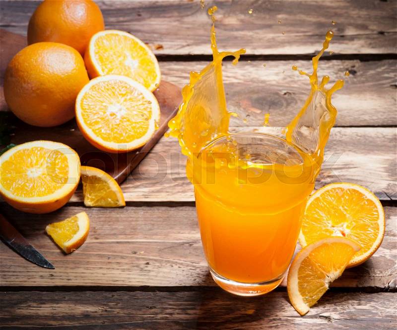 Glass of splashing orange juice on wood, stock photo