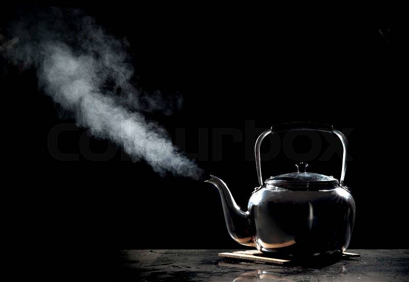 Tea kettle with boiling water on a black background, stock photo