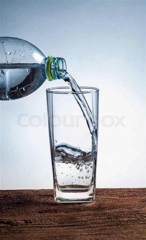 Water pouring from bottle into the glass on wood, stock photo