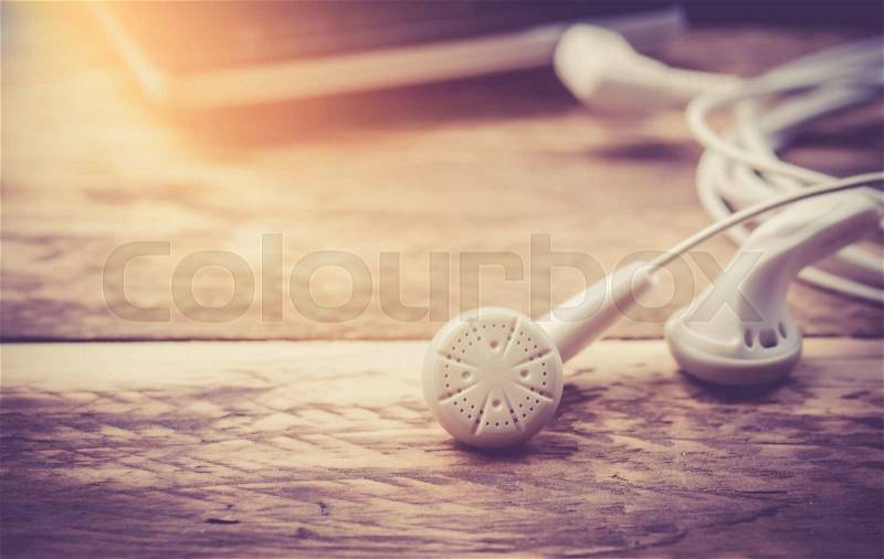 Earphones and Mobile phone on wooden background,vintage color toned image, stock photo