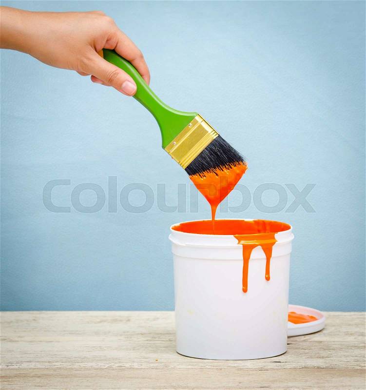 Hand holding the paint brush and White plastic bucket with orange color on wood,vintage background, stock photo