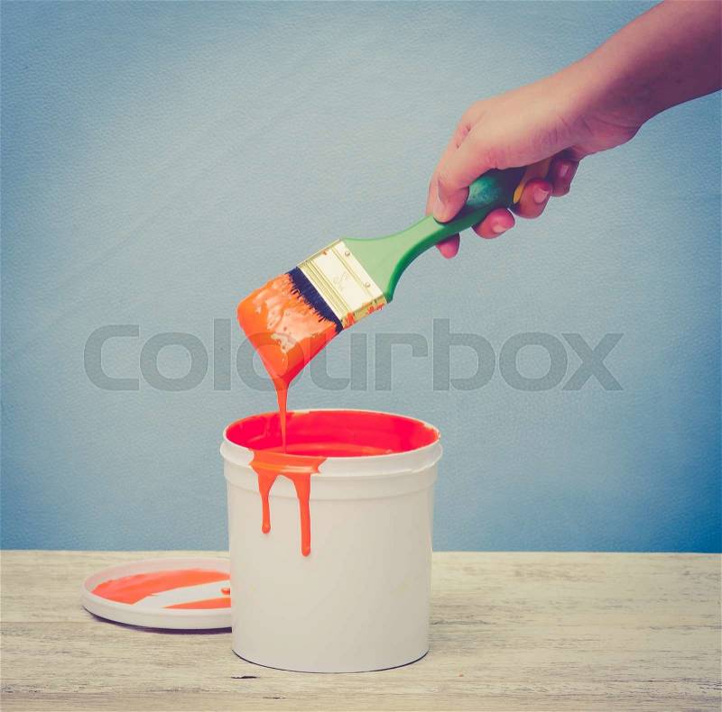 Hand holding the paint brush and White plastic bucket with orange color on wood,vintage color toned image, stock photo