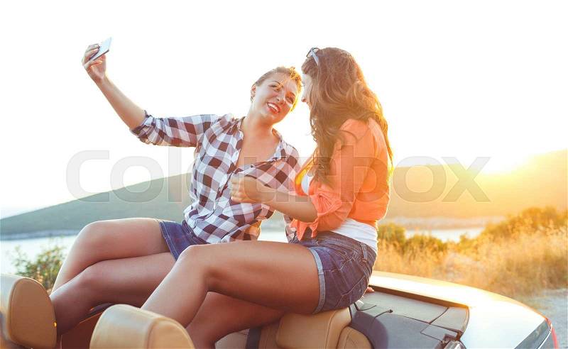 Two young beautiful girls are doing a photo of yourself in a convertible, stock photo