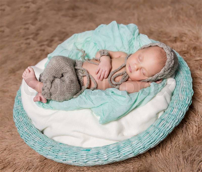 Newborn baby sleeping in round basket with knitted hat and toy, stock photo