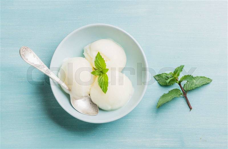 Lemon sorbet ice cream with mint bowl over turquoise blue background, top view, stock photo