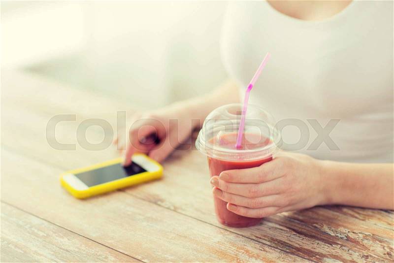 Healthy eating, diet, technology and people concept - close up of woman with smartphone and cup of smoothie sitting at table, stock photo