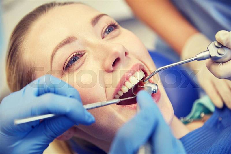 People, medicine, stomatology and health care concept - close up of dentists and assistant with mirror, drill and dental air water gun spray treating female patient teeth at dental clinic, stock photo