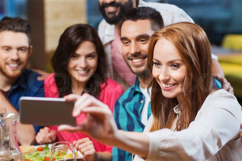 Leisure, technology, friendship, people and holidays concept - happy friends having dinner and taking selfie by smartphone at restaurant, stock photo