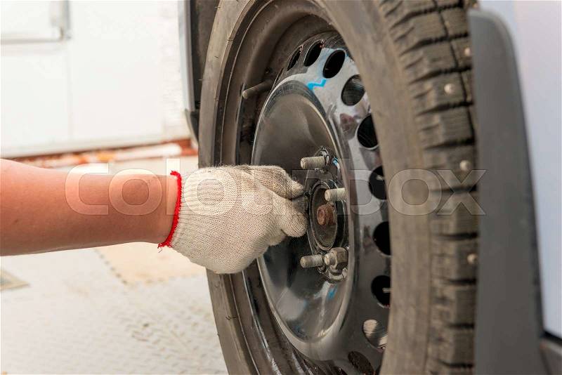 Man\'s hand tightening the screws on the wheel after installation, stock photo