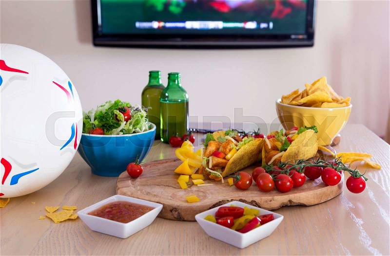 Mexican tacos and beer on a table with a football. There is a television in the background with sports showing, stock photo