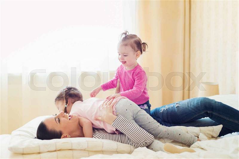 Beautiful young mother having fun with her daughters on bed in her bedroom, stock photo