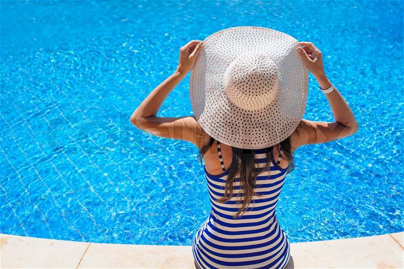 Beautiful woman in a hat sitting on the edge of the swimming pool, stock photo