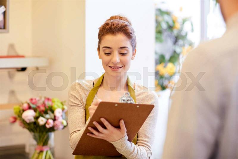 People, shopping, sale, floristry and consumerism concept - happy smiling florist woman with clipboard and man or customer making order at flower shop, stock photo