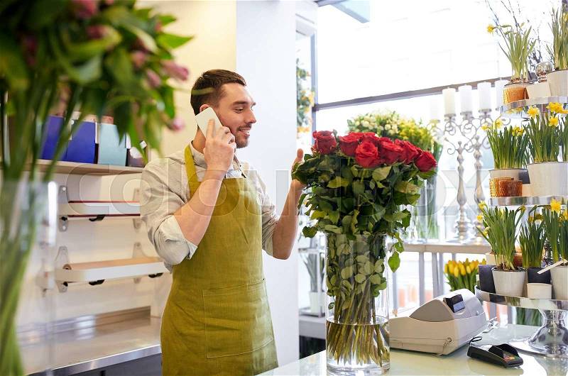 People, sale, retail, business and floristry concept - florist man with red roses calling on smartphone at flower shop counter, stock photo