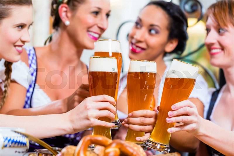 Girls toasting with wheat beer in Bavarian pub in front of pretzel, stock photo