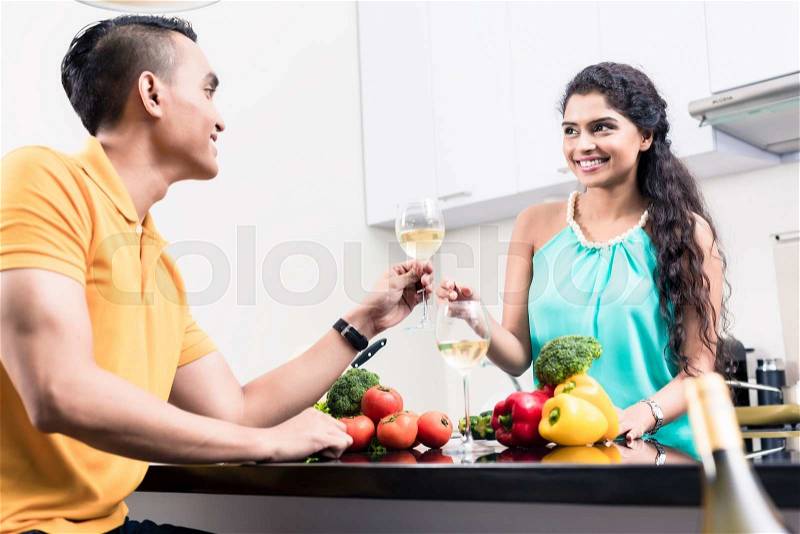 Indian woman and man in kitchen with red wine making salad, stock photo
