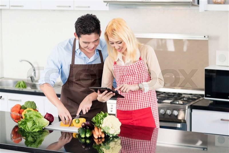 Asian couple cooking after recipes from tablet computer, stock photo