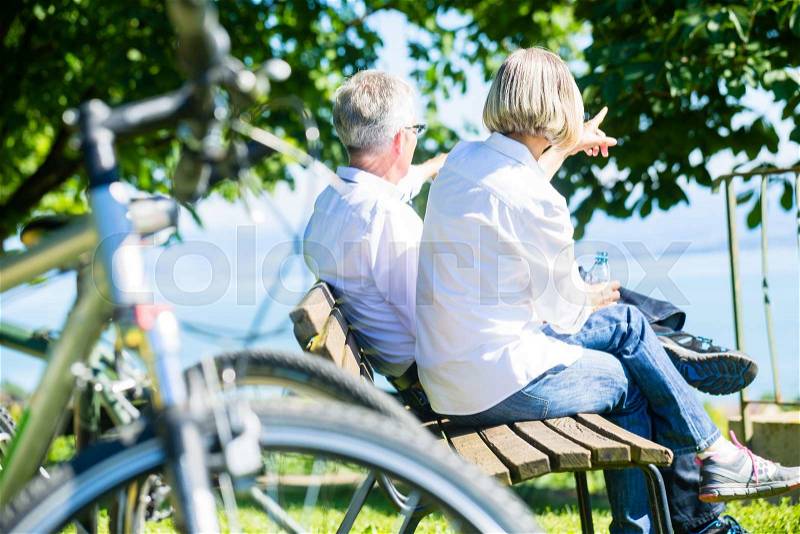 Senior woman and man at rest on bike trip sitting on a bench, stock photo