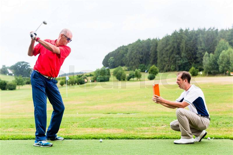 Golf trainer recording video of senior golf player, stock photo