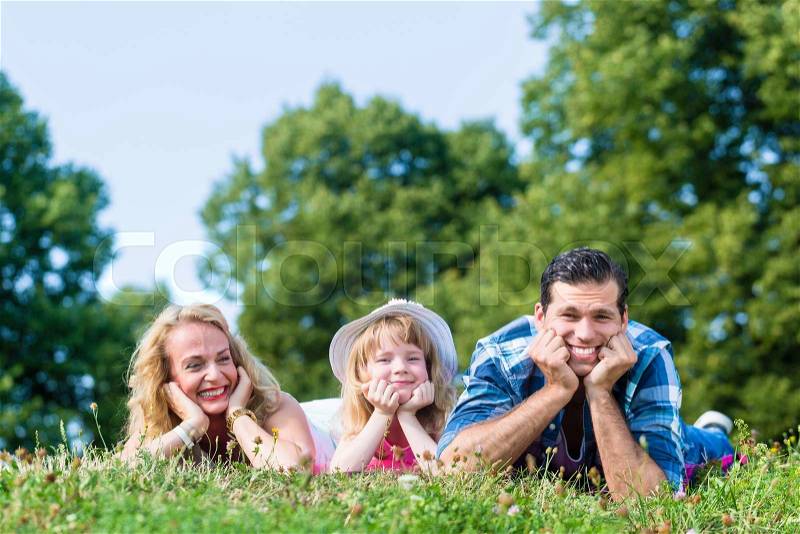 Family lying on meadow, looking to camera, cupping chins in hands, stock photo
