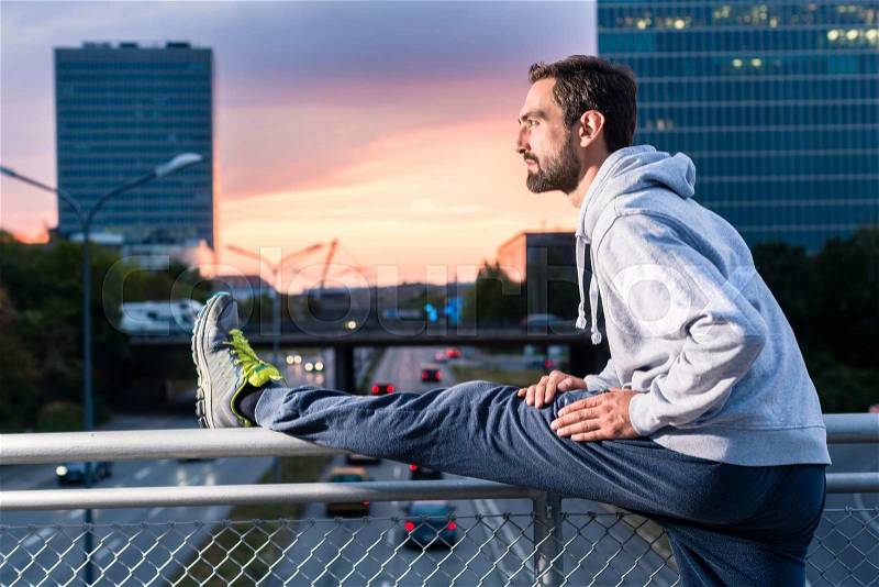 Runner stretching in front of office building at sunset, stock photo