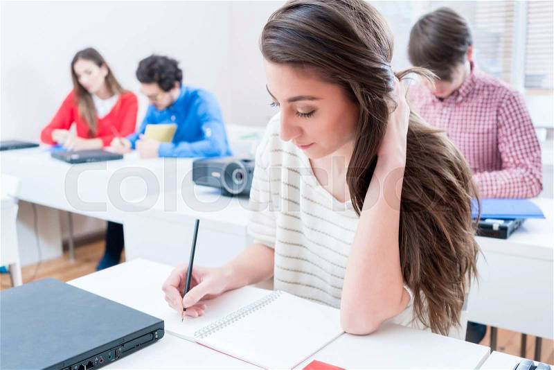 Student woman writing test in seminar room of university or having exam, stock photo