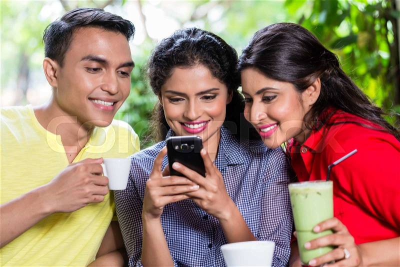 Indian girl showing pictures on smart phone to her friends in an Indian cafe, stock photo