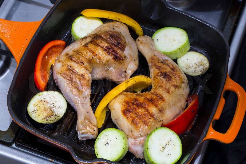 Cooking chicken legs and vegetables on the grill pan, stock photo