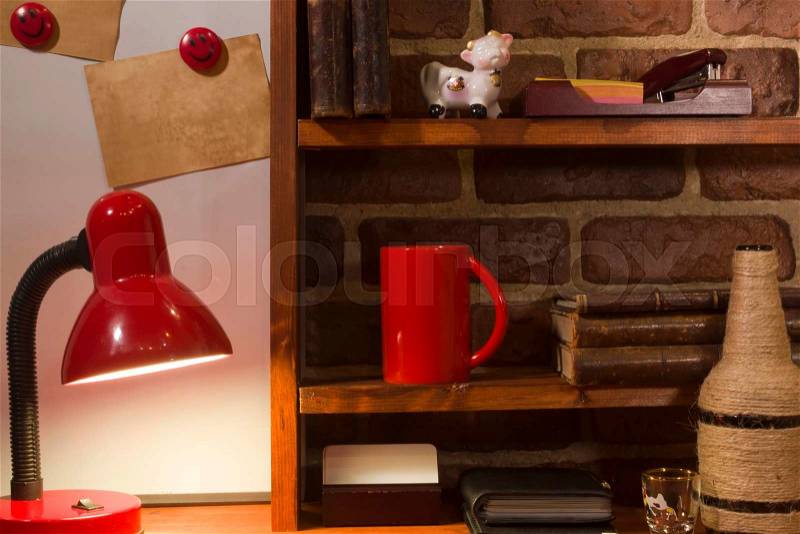 Vintage books coffee cup and desk lamp on the table. Wooden shelf on a background of the brickwork, stock photo