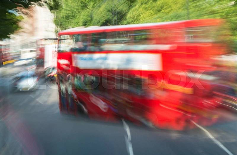 Fast moving red bus in London, framed by trees, stock photo